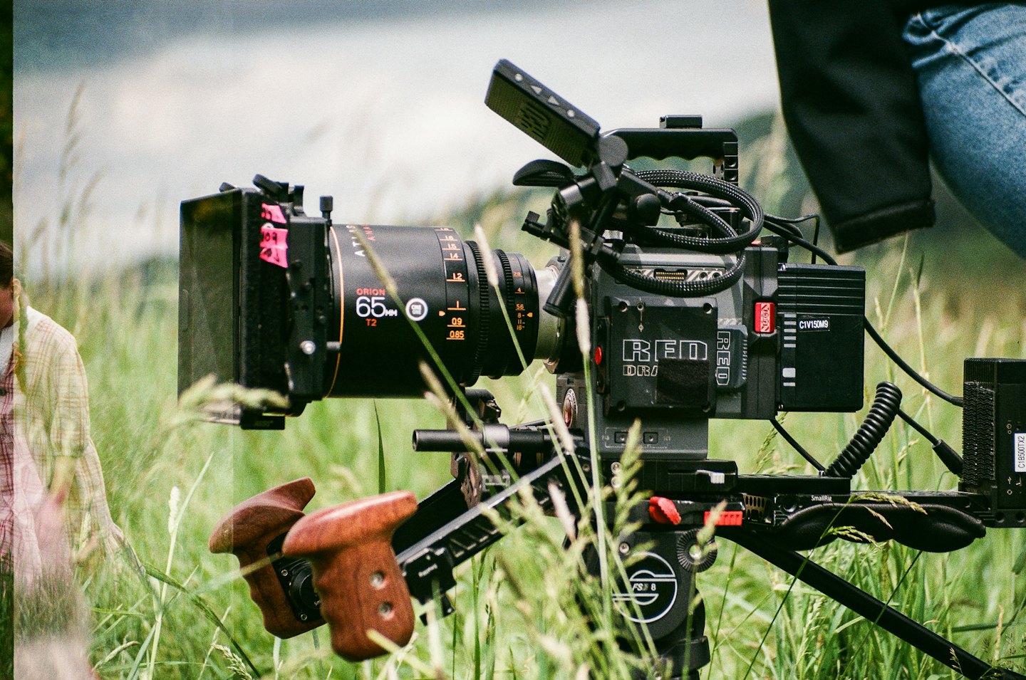 Professional cinema camera on a tripod in tall green grass.