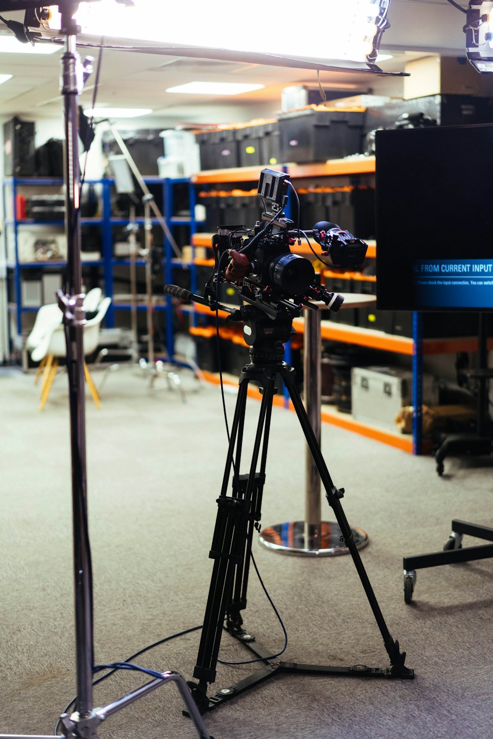 Professional video camera on a tripod inside a equipment warehouse.