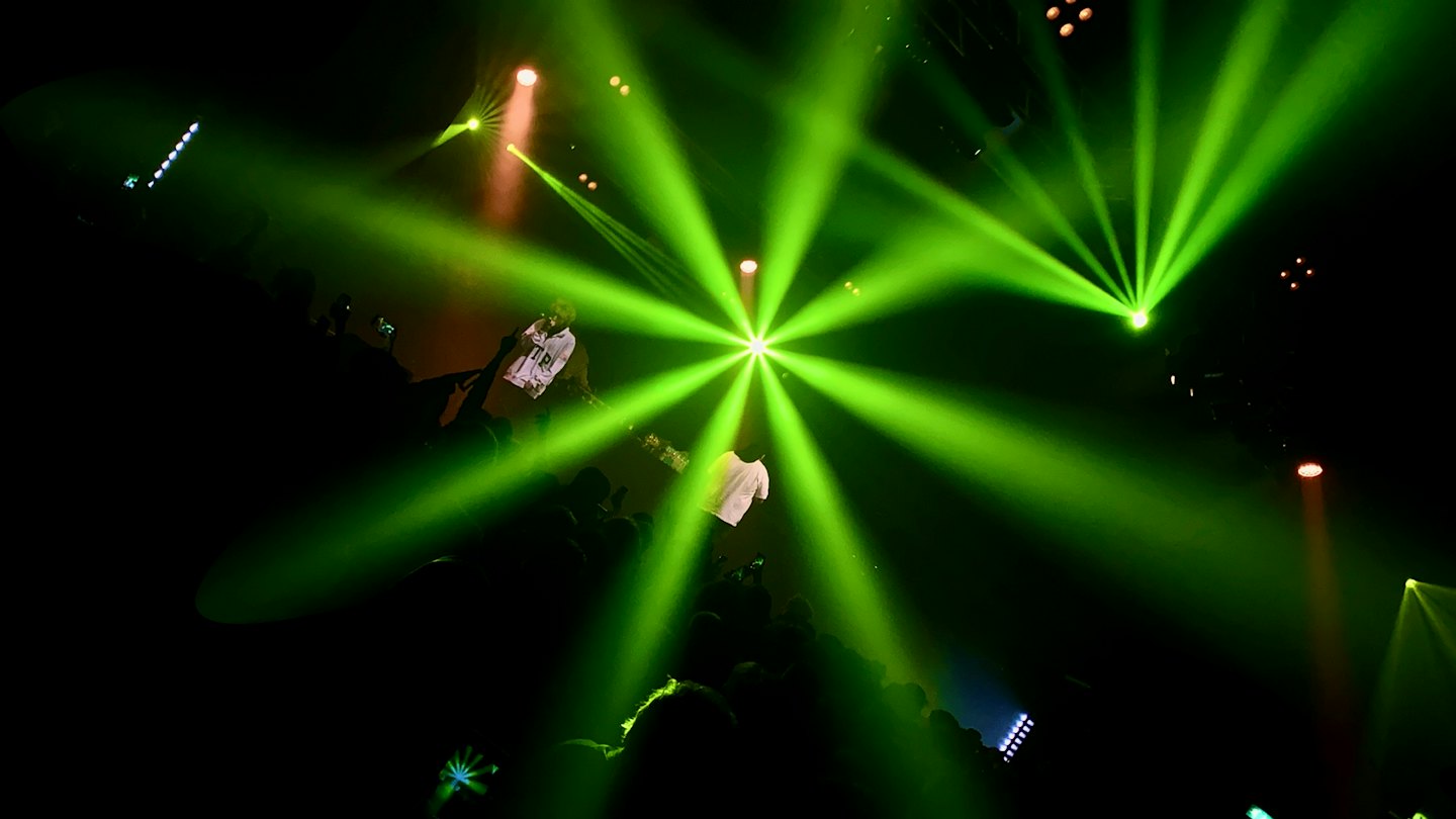 A performer on stage facing an audience holding up phones.